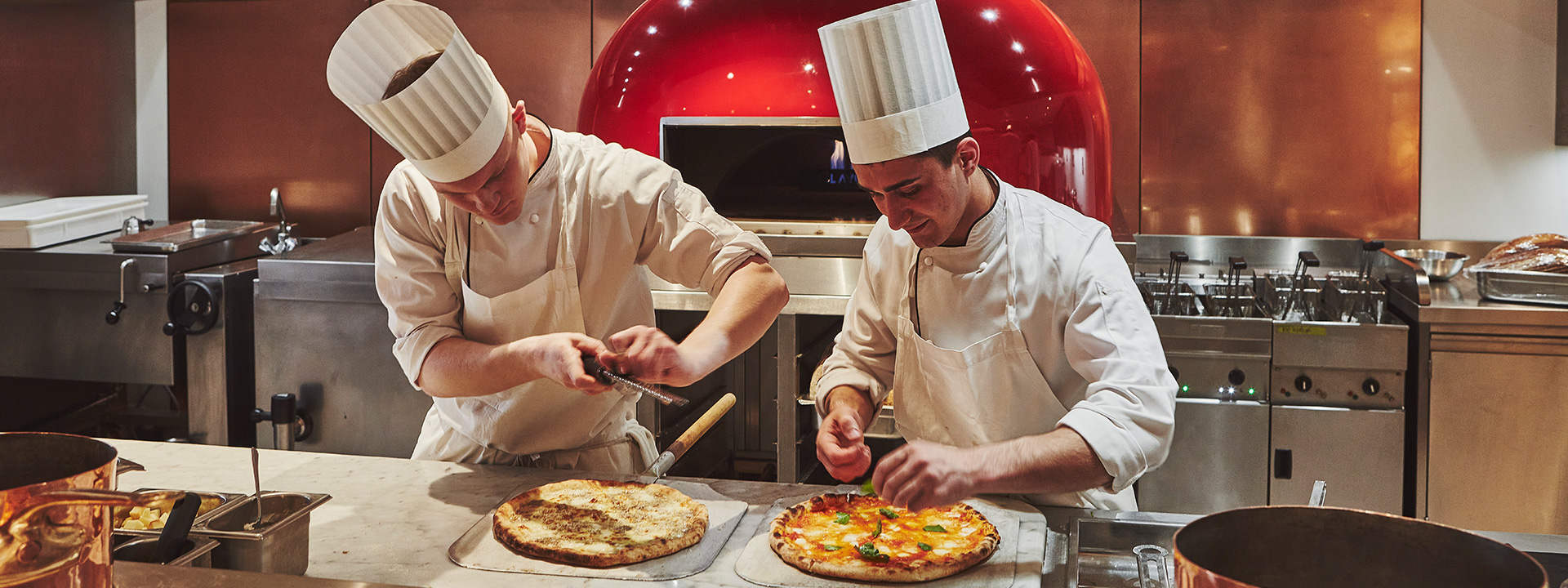 Photo of smiling and focused chefs preparing pizza and topping with parmesan cheese and garnish.