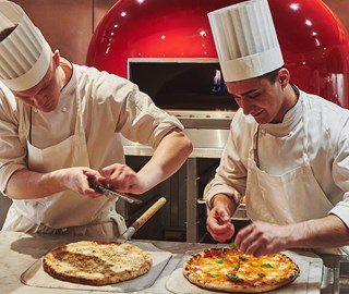 Two chefs cutting a stonebaked pizza in front of the pizza oven in L'Epicerie