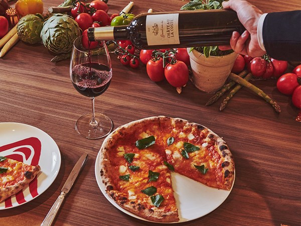 A display of wine is poured into a glass on a table in the L'Epicerie area, which also features delicious pizzas.