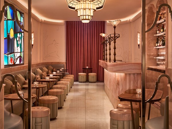 The Painter’s Room bar at Claridge’s, designed in soft pink and cream tones with art deco lighting, plush seating, and a striking stained-glass window.