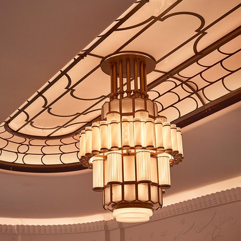 A detailed view of the large art deco chandelier with tiered frosted glass tubes and a geometric ceiling panel.