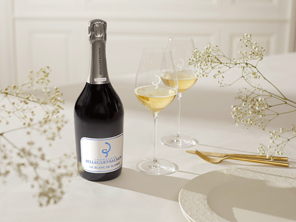 Bottle of Billecart-Salmon champagne with two filled glasses on a white table, styled with delicate flowers and place settings.