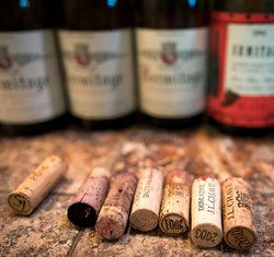 Several wine corks lined up on a surface with their respective bottles in the background, slightly out of focus. The corks and bottles suggest a tasting session featuring vintage wines.