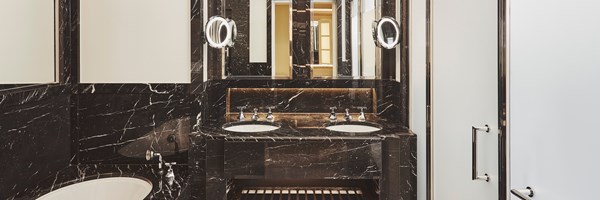 Claridges Brook Suite bathroom. Two marble sink sits in the middle ground and two mirrors sit above them. A marble bath is to the left.