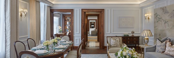 The dining and living room area with dining table and chairs and a sofa, and a view of the corridor with the bedroom in the background