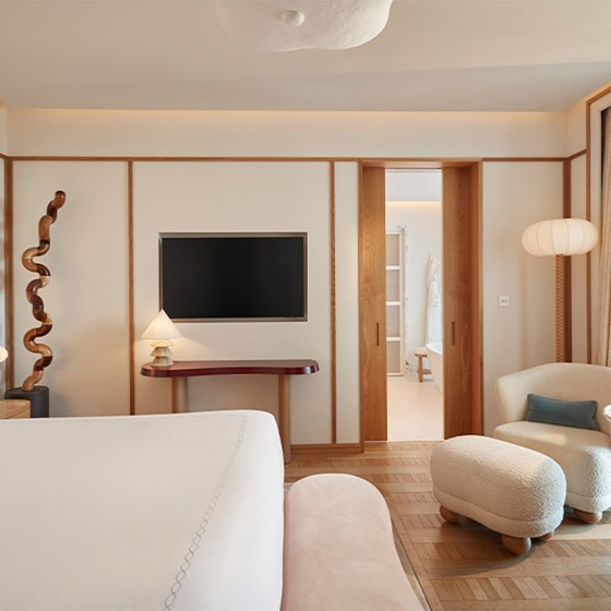 Inviting bedroom with a king-size bed, TV, armchair and stool, and wooden sliding doors opening to a marble-accented bathroom beyond.