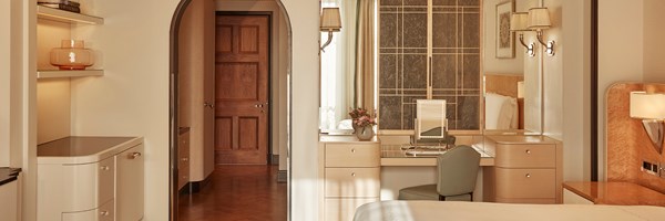 Elegant suite interior showing a dressing area with illuminated vanity mirror and desk, with an arched hallway and classic wooden door in the background.