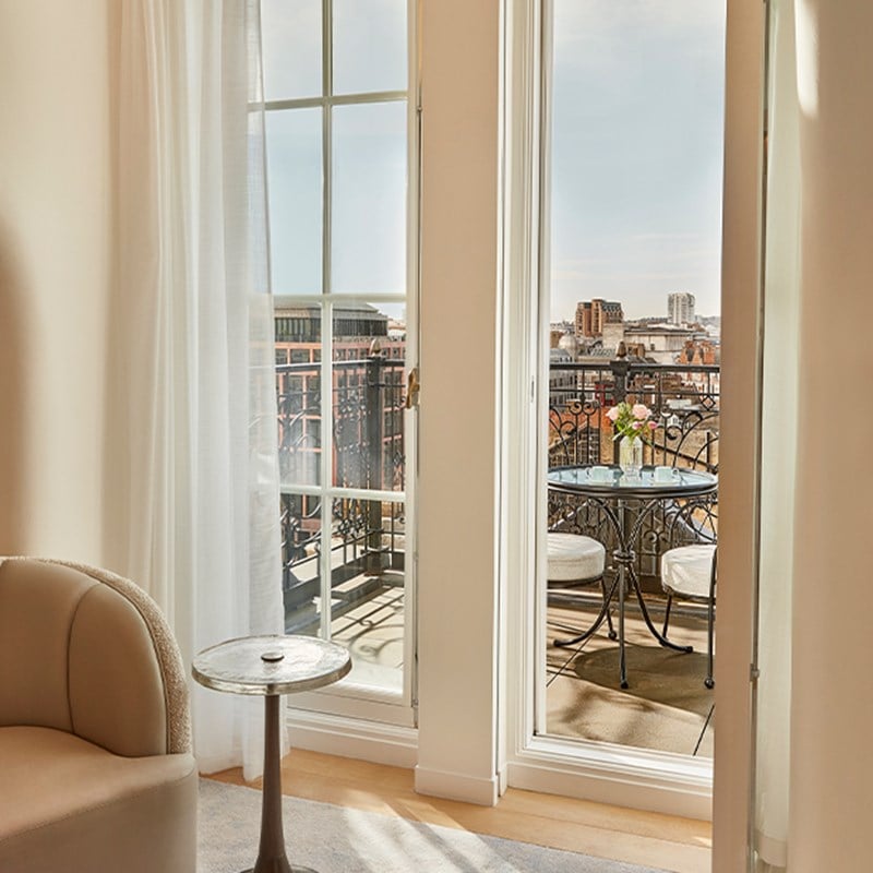 Small balcony setup with round table and chairs, offering skyline views over Mayfair rooftops through full-height windows.