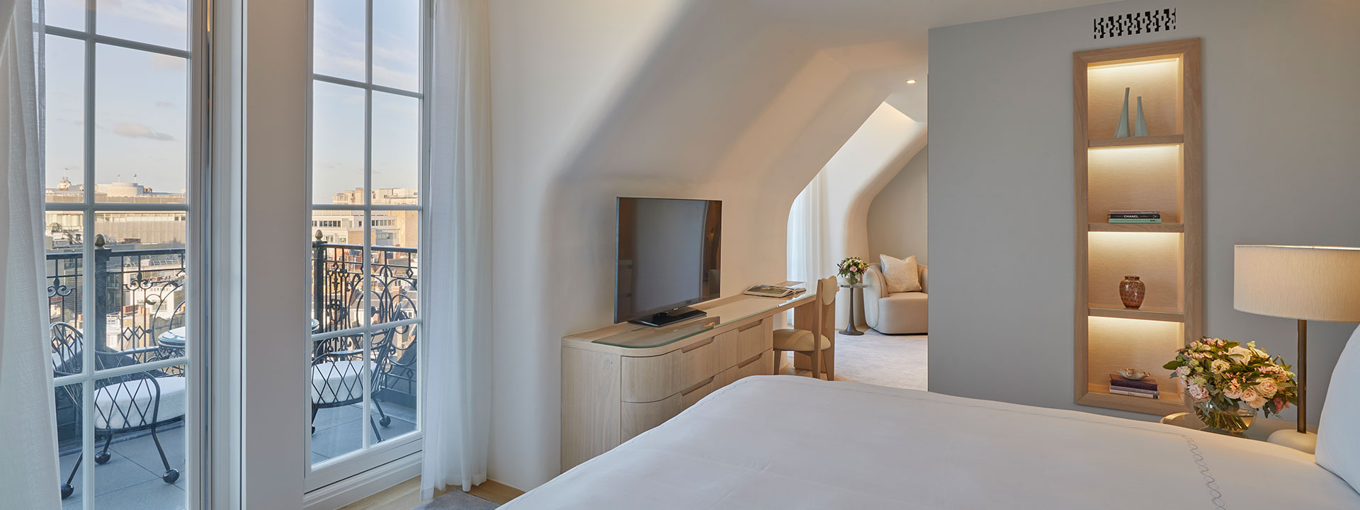 A view of the terrace from the bedroom in Claridge's Balcony Room, with a large TV and details in neutral tones.