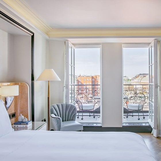 A view of the luxurious armchair and terrace, from the bedroom with one King Bed in Claridge's Balcony Room.