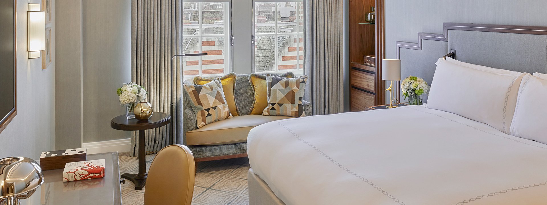 A view of a comfortable bedside sofa in a bedroom from Claridge's Room, with luxurious lamps and floral arrangements.