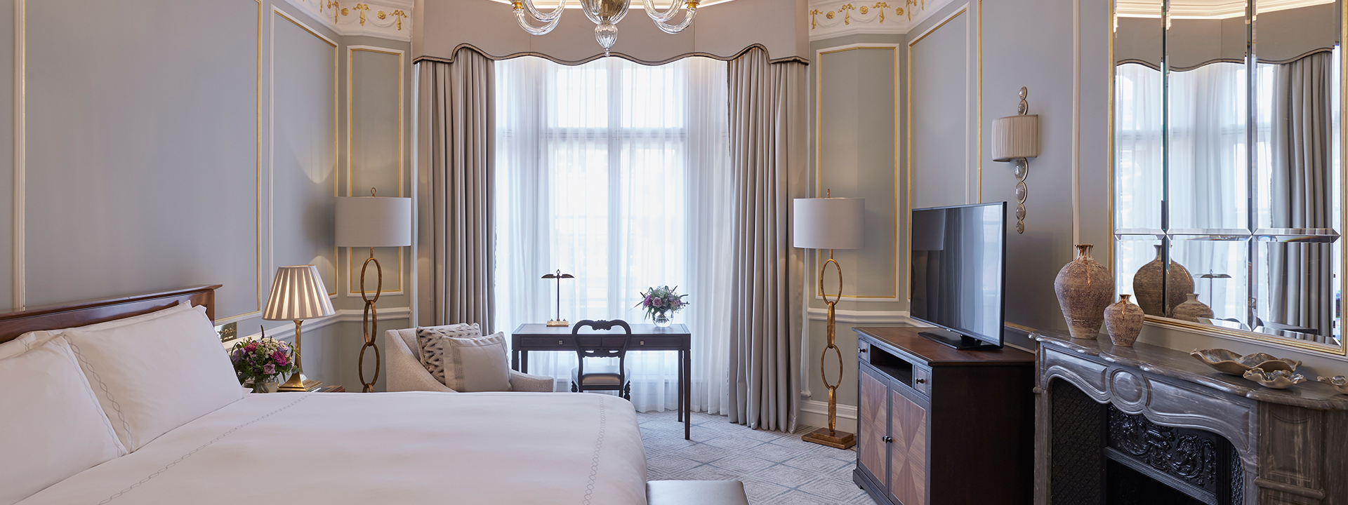 A comfortable bed and large TV in the bedroom from Claridge's Room, with luxurious lamps and vases in neutral colours.