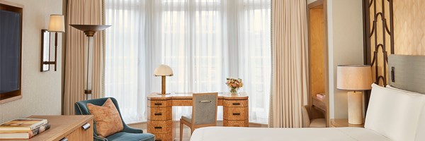 Bedroom with Art Deco details, cream curtains, a large window, and a mid-century inspired wooden desk and armchair.