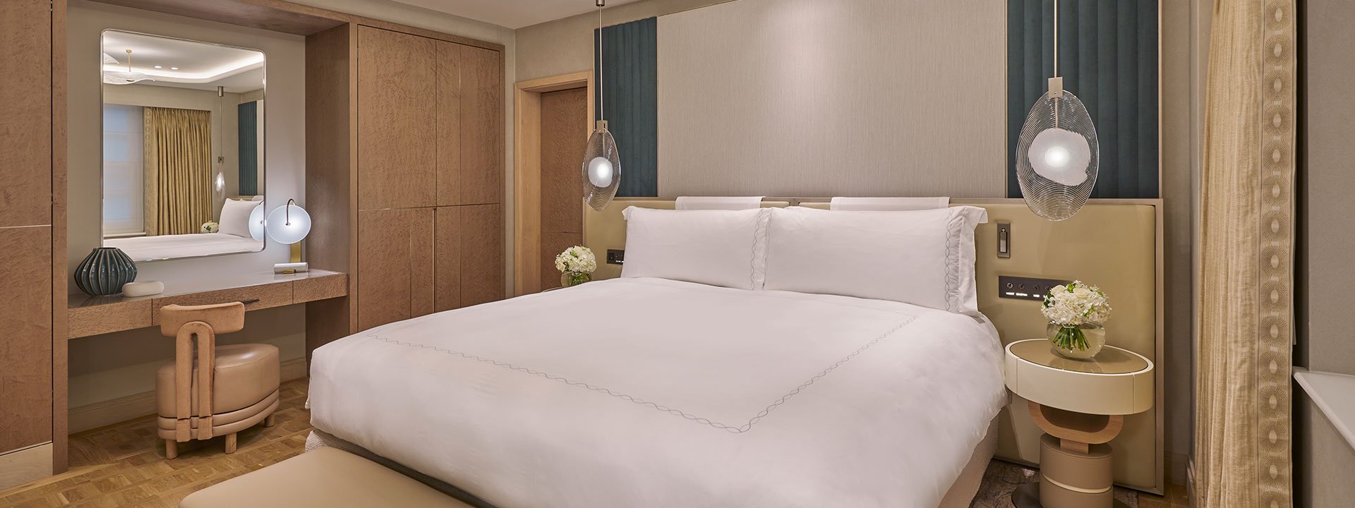 A modern bedroom in Claridge's Room, includes a King Bed, and luxurious panelling designed in a beige palette.