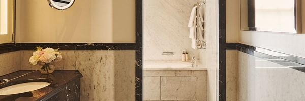 Luxurious marble bathroom featuring a built-in bathtub with chrome fixtures, folded white towels hanging on a heated rail, and a black marble countertop with a vase of pale pink and white flowers.