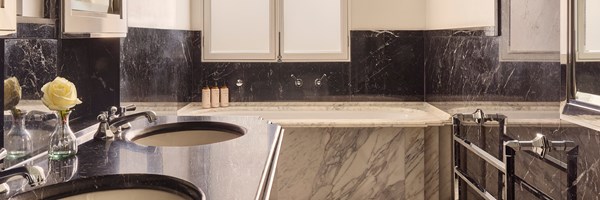Spacious bathroom with a black and white marble design, twin sinks, a deep soaking tub, and chrome towel rail beneath frosted windows.