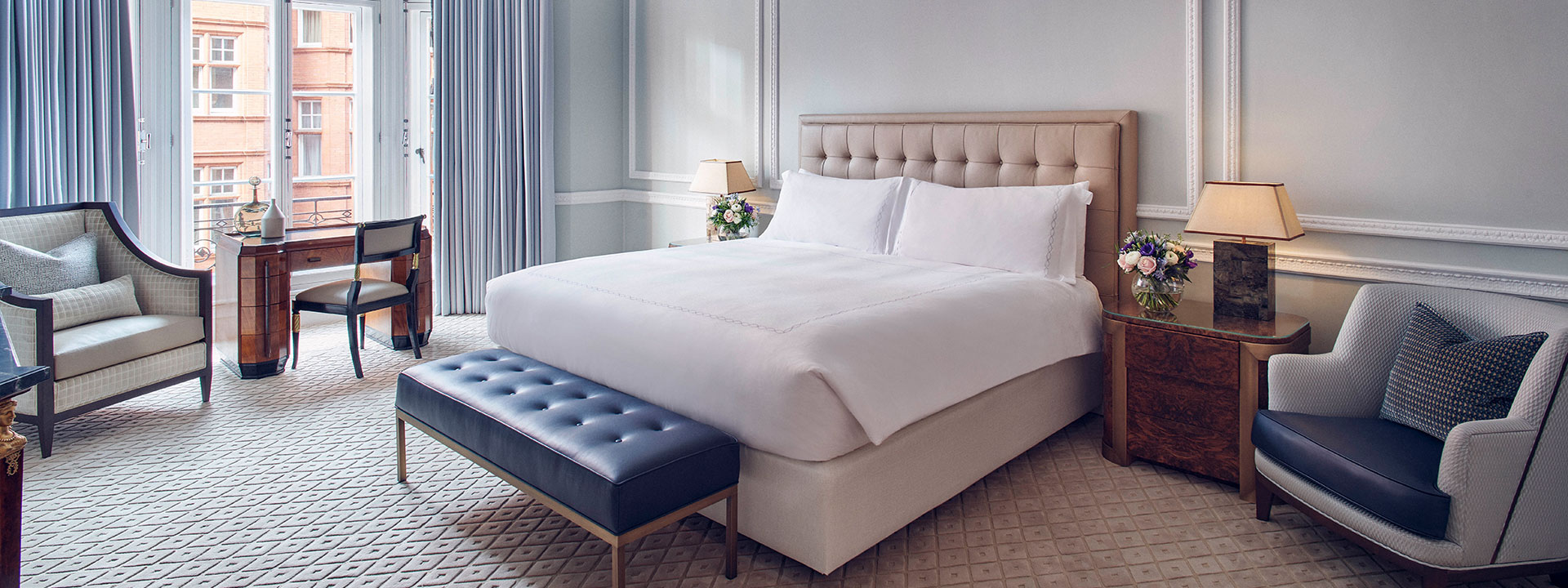 A view of the comfortable bed in the bedroom of the Corner Suite, complete with luxurious armchairs in natural daylight.