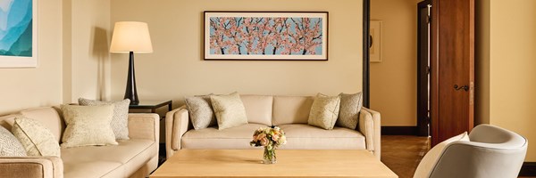 Elegant living room with two cream sofas, soft green cushions, and a light wood coffee table beneath artwork of cherry blossoms.