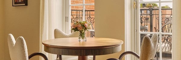 Dining nook with round wooden table, cream boucle chairs, and balcony view of red-brick architecture.