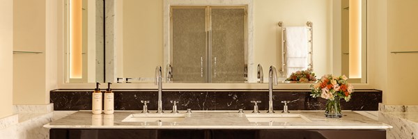 Marble bathroom vanity with twin basins, large mirror, and vase of fresh flowers beside luxury toiletries.