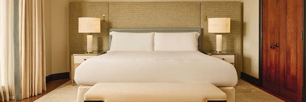 Bedroom with king-size bed, textured headboard, and matching bedside lamps framed by soft curtains.