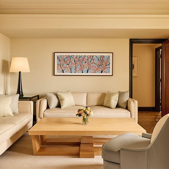 Wide view of the suite’s living area featuring neutral-toned sofas, light wood table, and framed cherry blossom artwork.