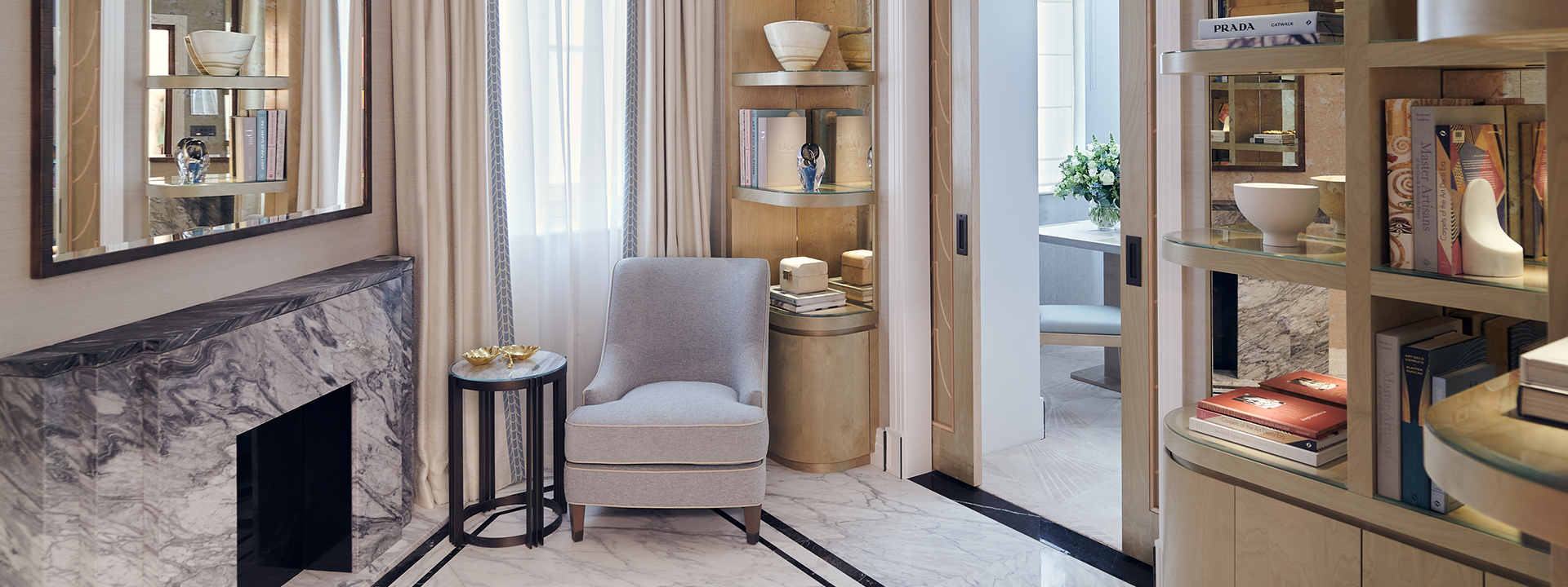 A comfortable grey armchair next to a marble fireplace, surrounded by luxurious details in the Deluxe Junior Suite.