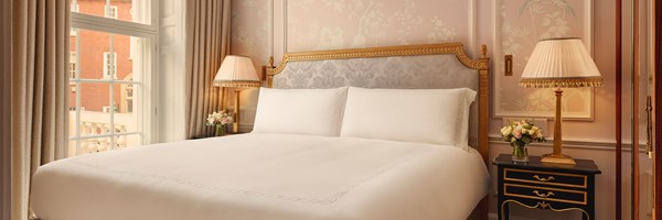 A Georgian-style bedroom with a grand gilded headboard, soft floral wallpaper, and bedside lamps on black and gold tables.