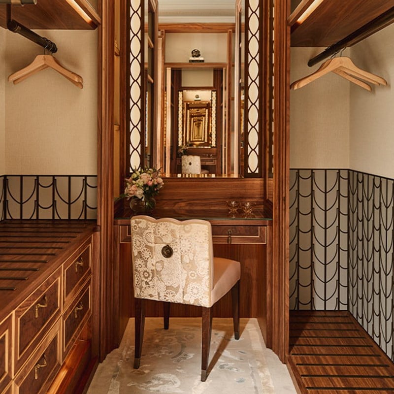 A wood-paneled dressing area with a vanity, upholstered chair, and mirrored walls.