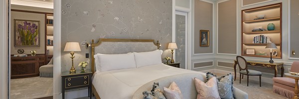 The bedroom at Claridge's with a double bed, bedside tables with lamps on the, a desk with a chair and a set of shelves.
