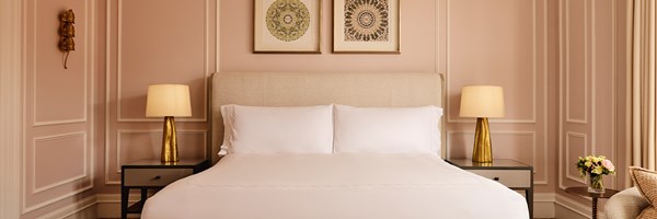 Elegant bedroom with a king-size bed, soft pink walls, golden lamps, and framed mandala artwork above the headboard.