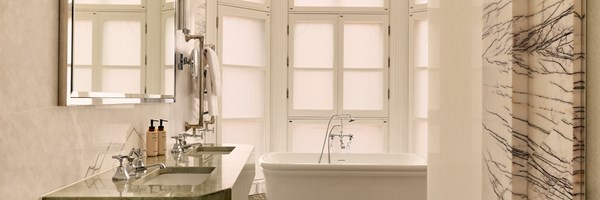 Luxurious bathroom with a freestanding bathtub, twin basins, marble accents, and tall frosted windows.