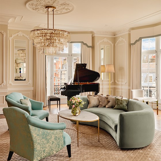 Cosy seating area with soft green armchairs and curved velvet sofa around a marble coffee table, lit by a crystal chandelier.