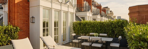 Private terrace of the Grand Terrace Suite with sun loungers, a dining table and chairs, and greenery screening against the backdrop of red-brick architecture.