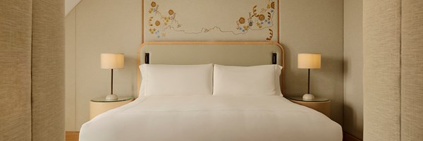 Bedroom in the Grand Terrace Suite with a king-size bed dressed in white linens, soft beige walls, and embroidered floral artwork above the headboard.