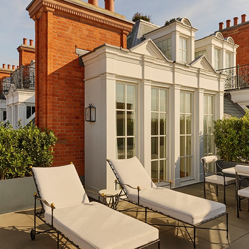 Private terrace of the Grand Terrace Suite with white sun loungers, a dining area, and red-brick architecture with French windows.