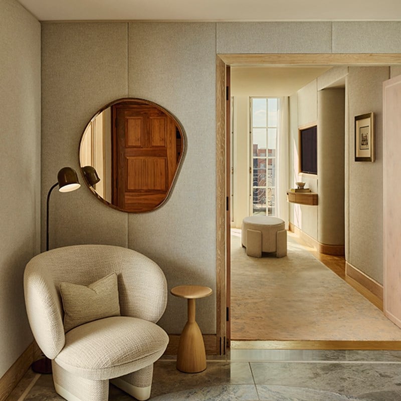 Hallway in the Grand Terrace Suite with a cream armchair, side table, and floor lamp, leading towards a light-filled lounge area with French doors.