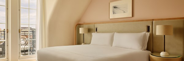 Second bedroom of the Grand Terrace Suite with a king-size bed, minimalist décor in warm tones, and French doors leading to a private balcony with city views.
