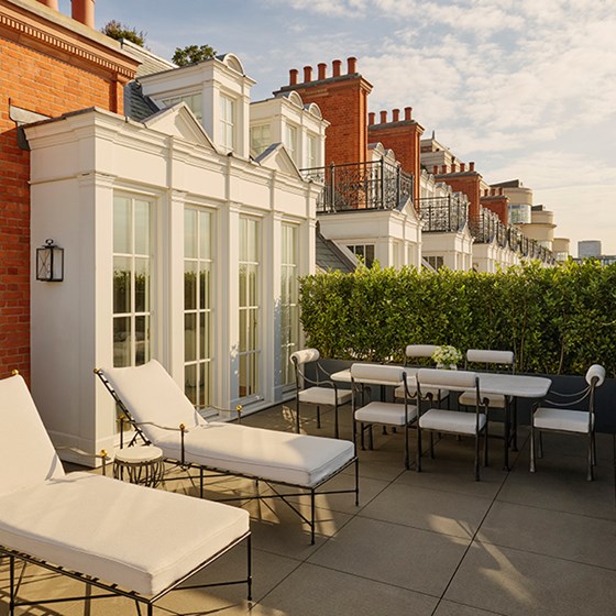 Private terrace of the Grand Terrace Suite with sun loungers, a dining table and chairs, and greenery screening against the backdrop of red-brick architecture.