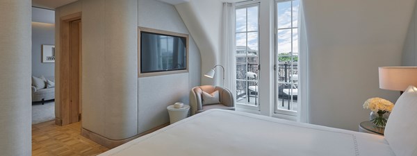 Bed with white bedding and doors opening to terrace of suite bedrom