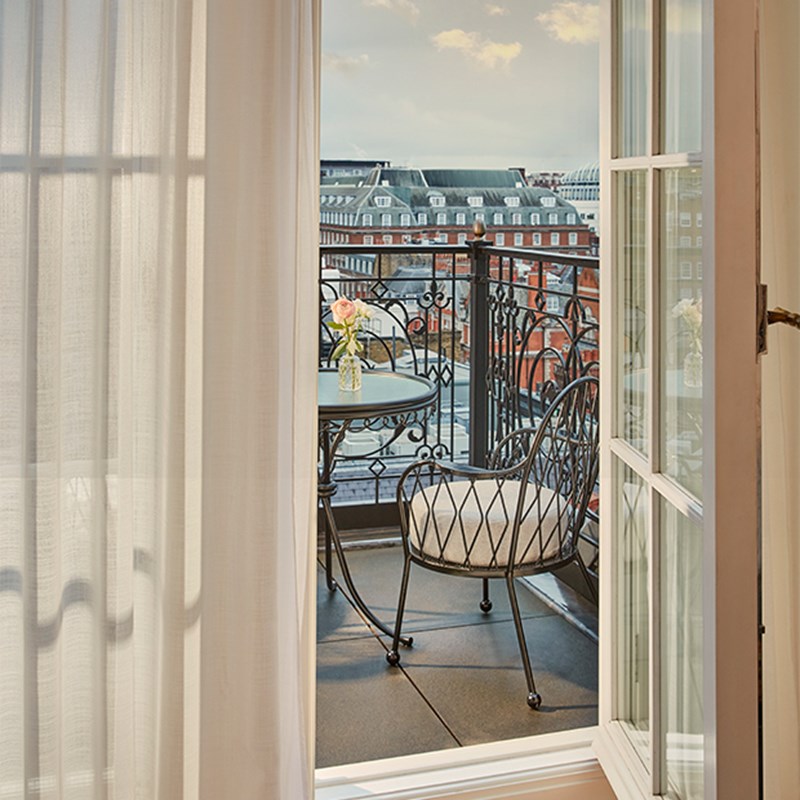 Elegant black metal balcony table and chair set framed by sheer curtains, overlooking Claridge’s rooftops and Mayfair skyline.