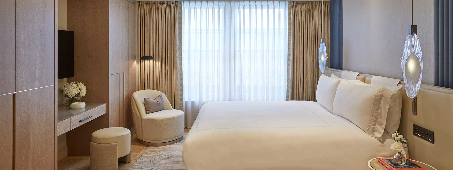 A bed and an armchair in the Mayfair Room, in a champagne-coloured interior with a subtle design.