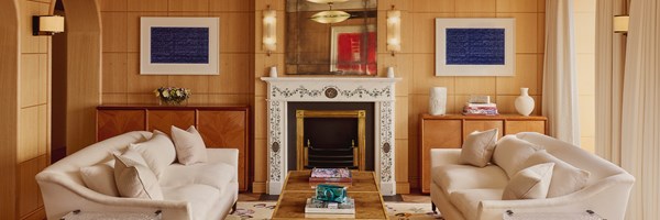Wide view of a symmetrical living room with two cream sofas, floral fireplace, and matching art on wood-panelled walls.