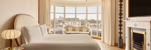 Bright bedroom with a curved floor-to-ceiling window, king-size bed, and modern cream loveseat.