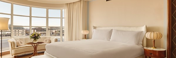 Spacious bedroom with a king-size bed, curved windows, plush seating, and skyline views.