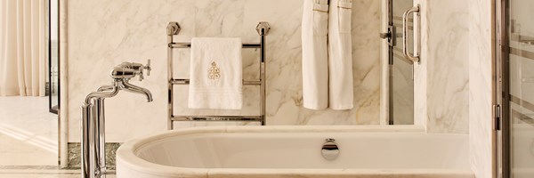 Elegant marble bathroom with freestanding bathtub, chrome fittings, and luxury embroidered towels on a heated rail.