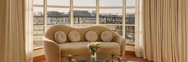 Curved cream sofa and round glass coffee table positioned beside wide bay windows, flooding the room with natural light.