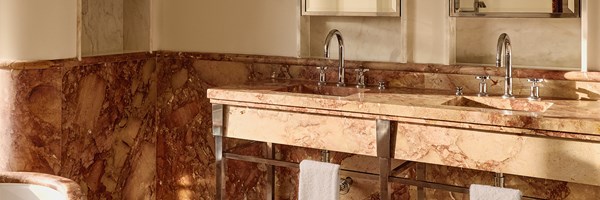 Luxurious marble bathroom with double sinks, polished chrome fittings, and soft natural light casting warm tones across the stone.