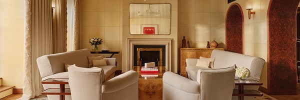 A spacious, elegant living room with four cream armchairs, fireplace, and soft lighting, creating a warm, intimate setting.