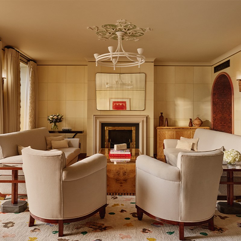 Bright, inviting living area featuring four armchairs arranged around a coffee table, with fireplace, books, mirror, and neutral-toned decor.